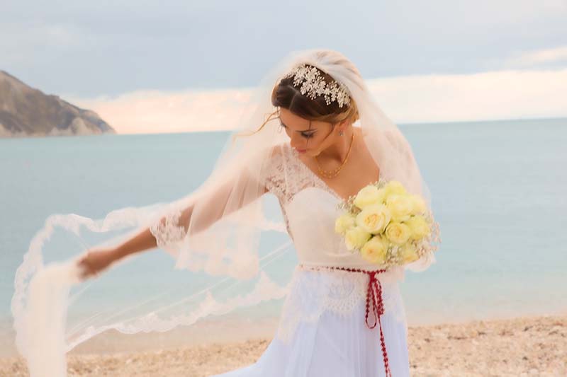 Una sposa gioca con l'abito mosso dal vento nella spiaggia di Portonovo, Ancona